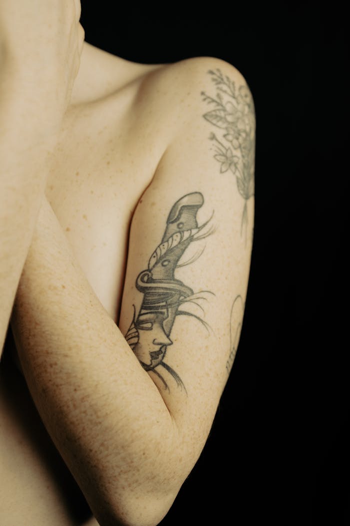 Close-up of a woman's arm adorned with intricate tattoos, featuring a black backdrop.
