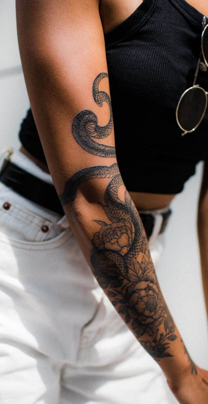 Close-up of a woman's tattooed arm with snake and floral design. Perfect for fashion and lifestyle themes.