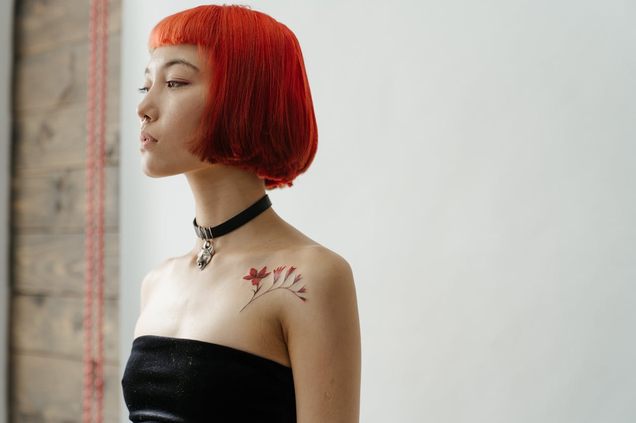 Portrait of a fashionable woman with red hair and shoulder tattoo in a studio setting.